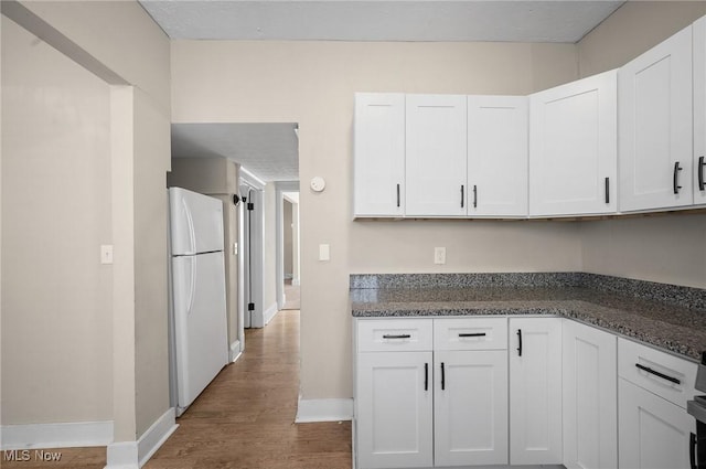 kitchen with white cabinets, dark stone counters, freestanding refrigerator, and wood finished floors