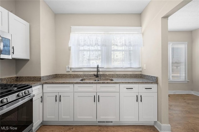 kitchen with a sink, stainless steel gas range oven, and white cabinets