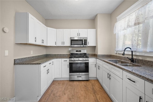 kitchen with a sink, dark stone countertops, white cabinetry, appliances with stainless steel finishes, and light wood finished floors