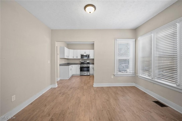 unfurnished dining area featuring light wood-type flooring, visible vents, baseboards, and a textured ceiling