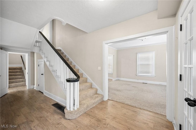 staircase featuring visible vents, baseboards, a textured ceiling, and wood finished floors