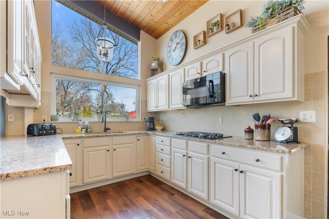 kitchen with black microwave, stainless steel gas cooktop, dark wood finished floors, wooden ceiling, and a sink