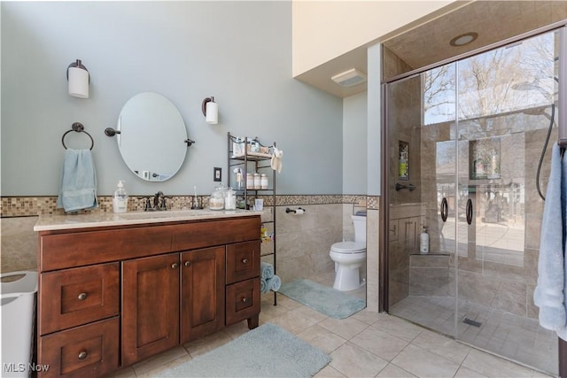 full bathroom featuring vanity, a stall shower, tile walls, toilet, and tile patterned floors