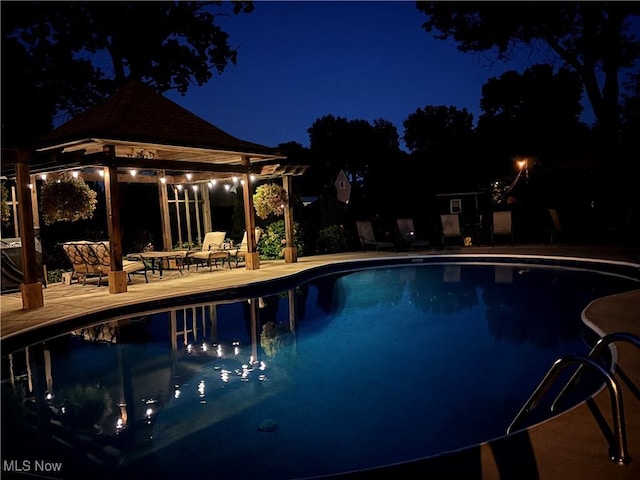 pool at night featuring a gazebo, a patio, and an outdoor pool