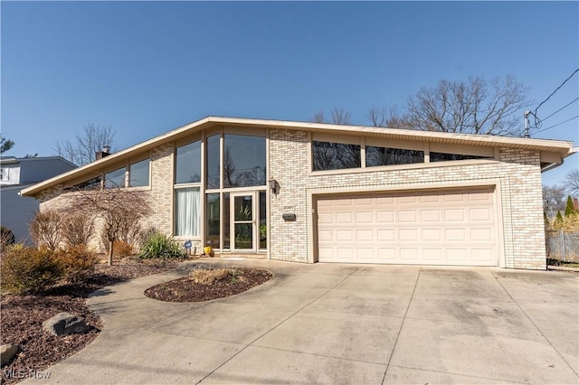 mid-century modern home with brick siding, an attached garage, and concrete driveway