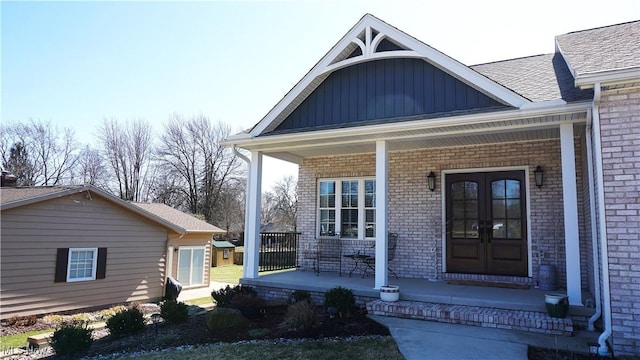 doorway to property with brick siding, covered porch, french doors, and board and batten siding