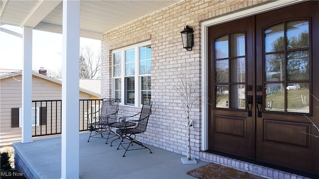 entrance to property featuring a porch, french doors, and brick siding