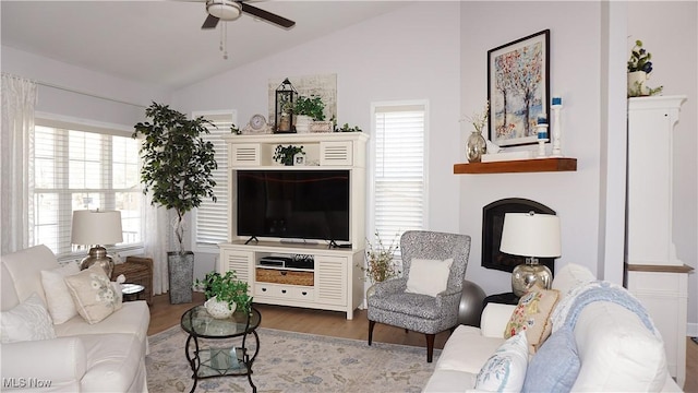 living area featuring a fireplace, wood finished floors, a ceiling fan, and vaulted ceiling