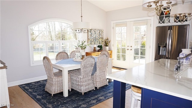 dining room featuring a healthy amount of sunlight, a chandelier, lofted ceiling, french doors, and wood finished floors