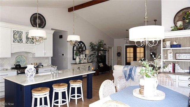 kitchen featuring wood finished floors, a sink, beamed ceiling, backsplash, and a chandelier