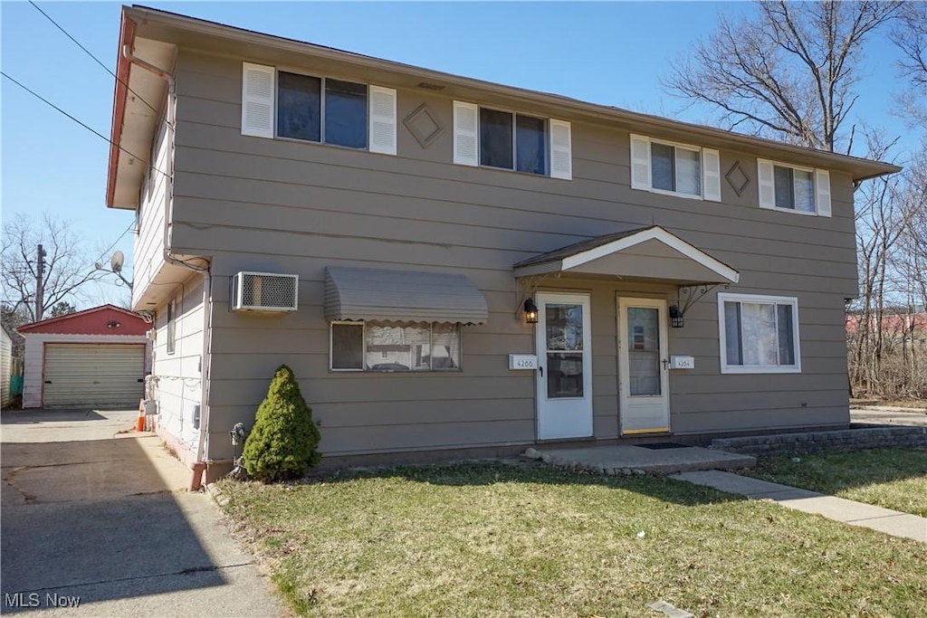 view of front of property featuring driveway, a front lawn, a wall mounted AC, an outdoor structure, and a garage