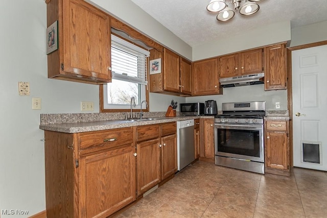 kitchen featuring brown cabinets, a notable chandelier, under cabinet range hood, a sink, and appliances with stainless steel finishes