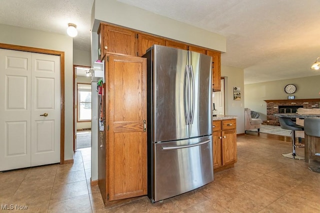 kitchen featuring a textured ceiling, open floor plan, brown cabinetry, and freestanding refrigerator