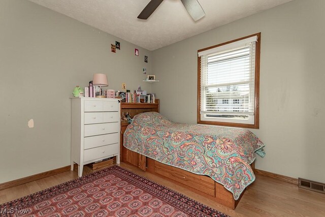 bedroom with visible vents, a textured ceiling, wood finished floors, baseboards, and ceiling fan