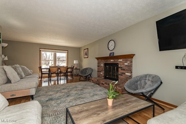 living area with a fireplace, a textured ceiling, baseboards, and wood finished floors