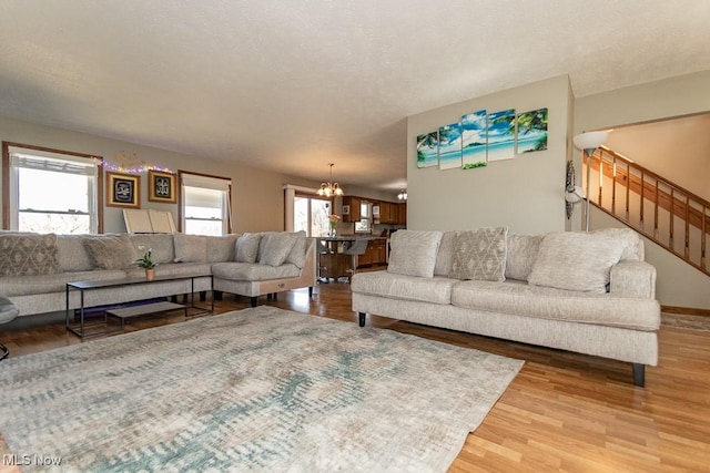 living room with a chandelier, light wood finished floors, stairs, and baseboards