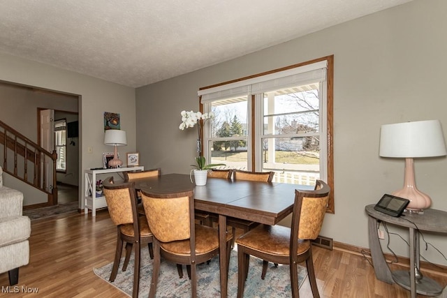 dining area with visible vents, a textured ceiling, wood finished floors, stairway, and baseboards