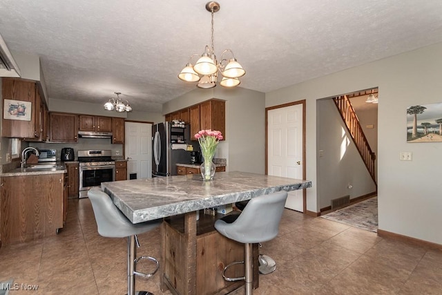 kitchen featuring baseboards, a sink, stainless steel appliances, under cabinet range hood, and a chandelier