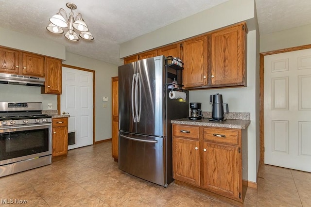 kitchen with under cabinet range hood, a textured ceiling, appliances with stainless steel finishes, brown cabinetry, and a chandelier