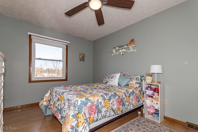 bedroom with visible vents, baseboards, a textured ceiling, and wood finished floors