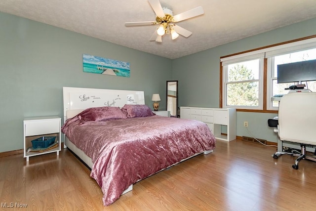 bedroom featuring a ceiling fan, wood finished floors, baseboards, and a textured ceiling