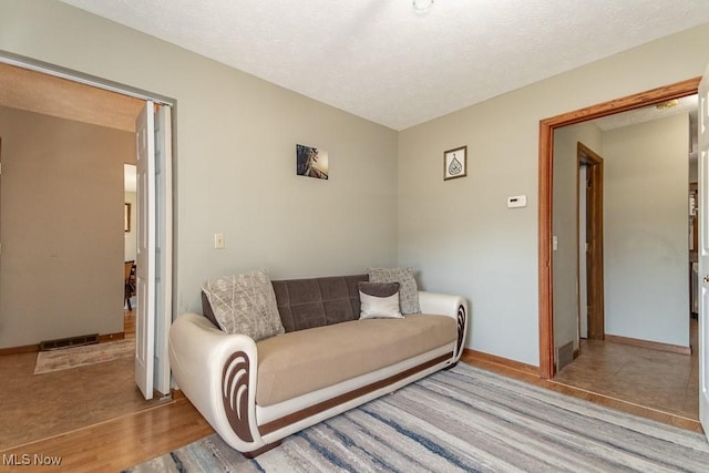 living room with visible vents, baseboards, a textured ceiling, and wood finished floors