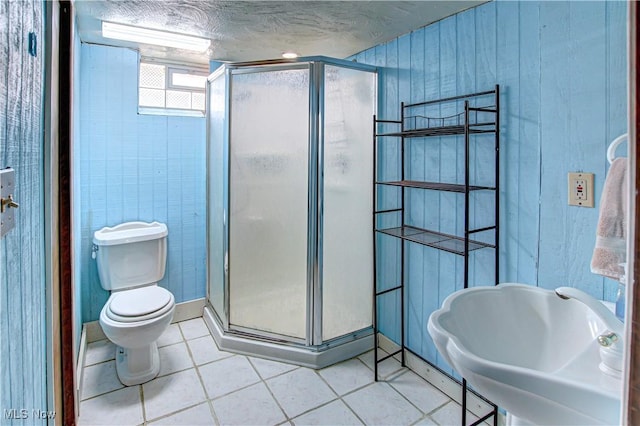 bathroom featuring toilet, a sink, a textured ceiling, a shower stall, and tile patterned flooring