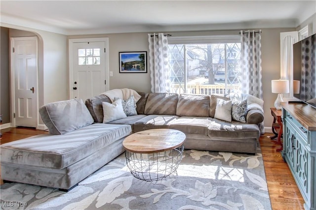 living area with baseboards, arched walkways, and wood finished floors