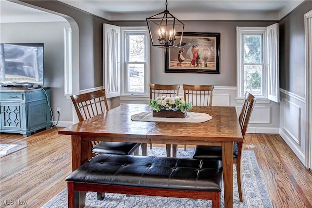 dining room featuring light wood-type flooring, wainscoting, an inviting chandelier, arched walkways, and a decorative wall