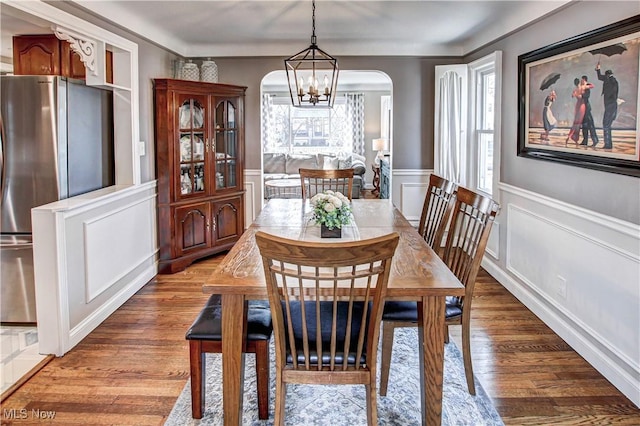 dining area with wainscoting, an inviting chandelier, wood finished floors, arched walkways, and a decorative wall