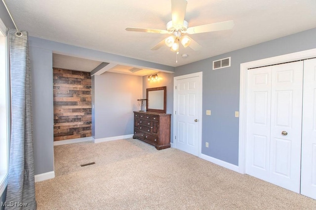 unfurnished bedroom with a closet, visible vents, wooden walls, and carpet floors