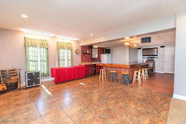 kitchen with a breakfast bar area, baseboards, recessed lighting, freestanding refrigerator, and a sink