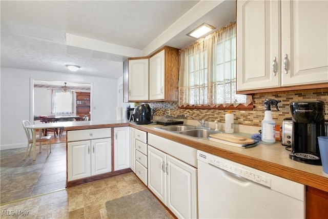 kitchen featuring a sink, backsplash, a peninsula, white dishwasher, and light countertops