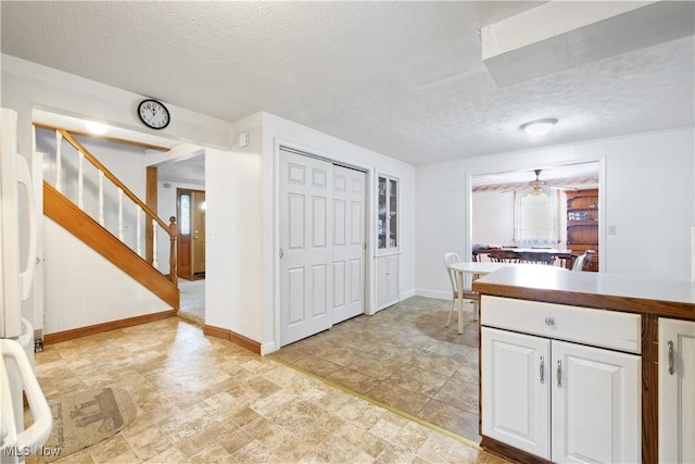 kitchen with baseboards, a textured ceiling, white cabinetry, and ceiling fan