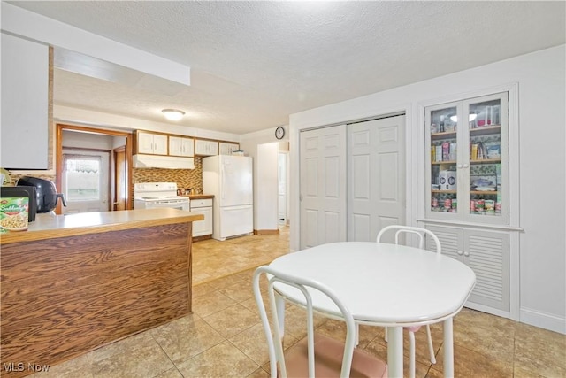 kitchen featuring white appliances, light tile patterned floors, decorative backsplash, under cabinet range hood, and a textured ceiling