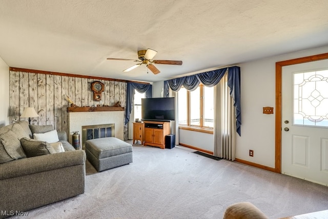 living area with baseboards, a fireplace, ceiling fan, a textured ceiling, and light colored carpet