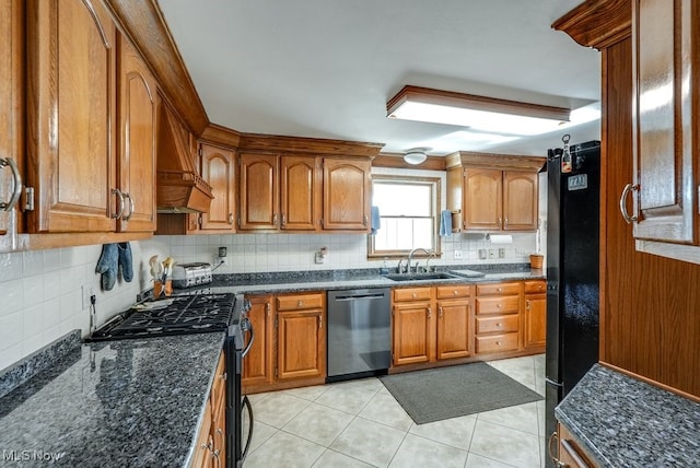 kitchen with a sink, dark stone countertops, appliances with stainless steel finishes, brown cabinetry, and decorative backsplash