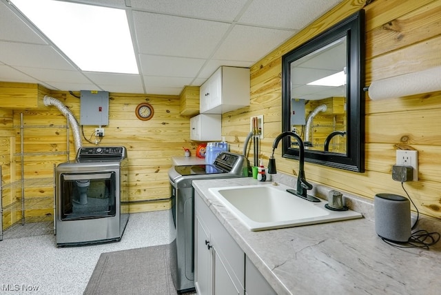 laundry room with electric panel, cabinet space, a sink, wood walls, and washer and clothes dryer