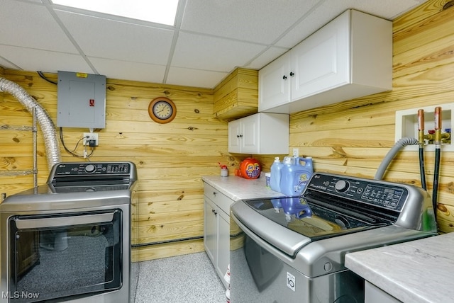 laundry room featuring electric panel, wooden walls, cabinet space, and washing machine and dryer