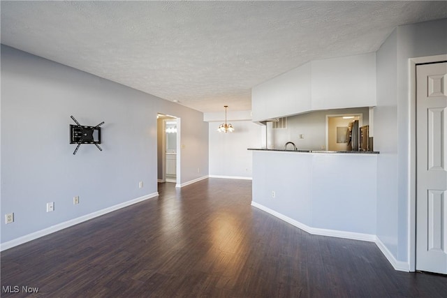 unfurnished living room with a notable chandelier, a textured ceiling, dark wood-type flooring, and baseboards