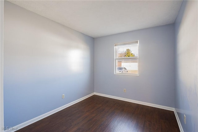 unfurnished room featuring baseboards and dark wood-style flooring