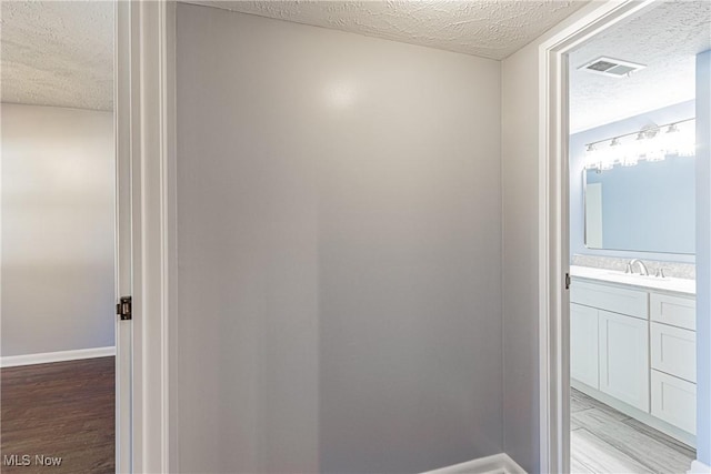 bathroom with vanity, wood finished floors, baseboards, visible vents, and a textured ceiling