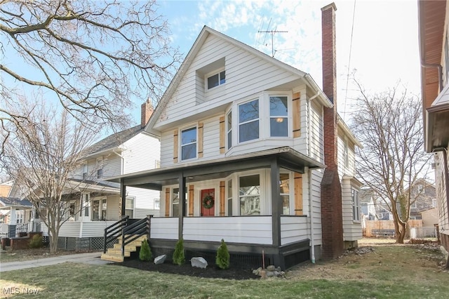 american foursquare style home with a front lawn, covered porch, and a chimney