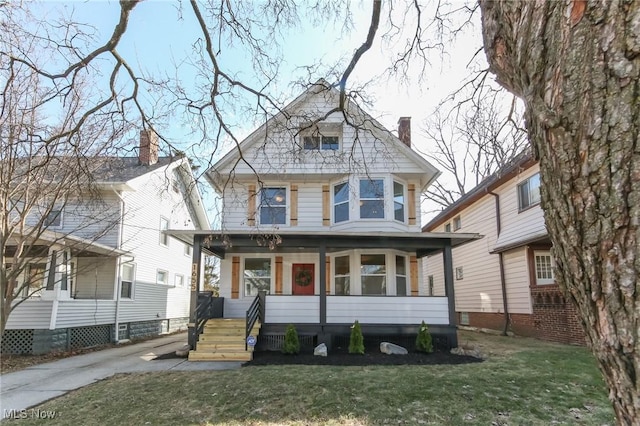 american foursquare style home featuring covered porch, a chimney, and a front yard