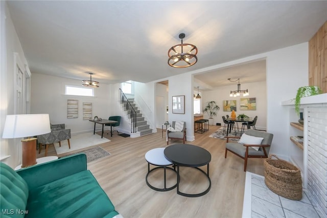 living area with stairs, an inviting chandelier, baseboards, and light wood finished floors