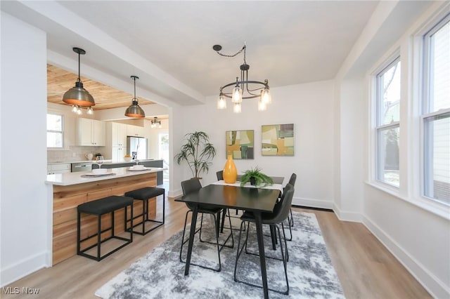 dining room with a notable chandelier, beamed ceiling, light wood-type flooring, and baseboards