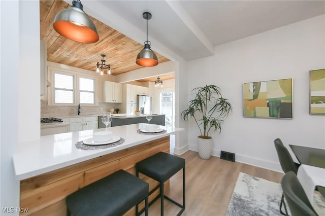 kitchen with stainless steel refrigerator with ice dispenser, a sink, white cabinetry, light countertops, and wood ceiling