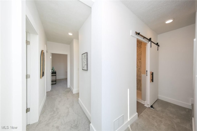 corridor featuring visible vents, baseboards, a barn door, light carpet, and a textured ceiling