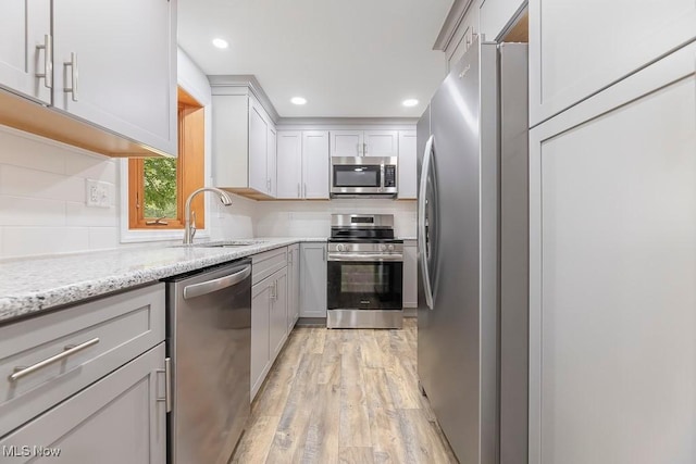 kitchen featuring light stone countertops, light wood-type flooring, a sink, appliances with stainless steel finishes, and tasteful backsplash