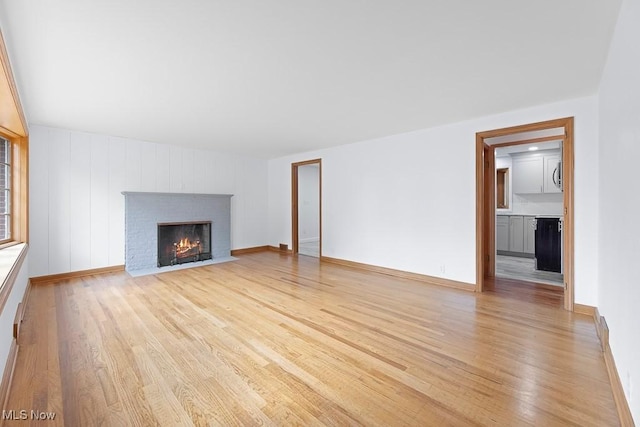 unfurnished living room featuring baseboards, a brick fireplace, and light wood-style flooring